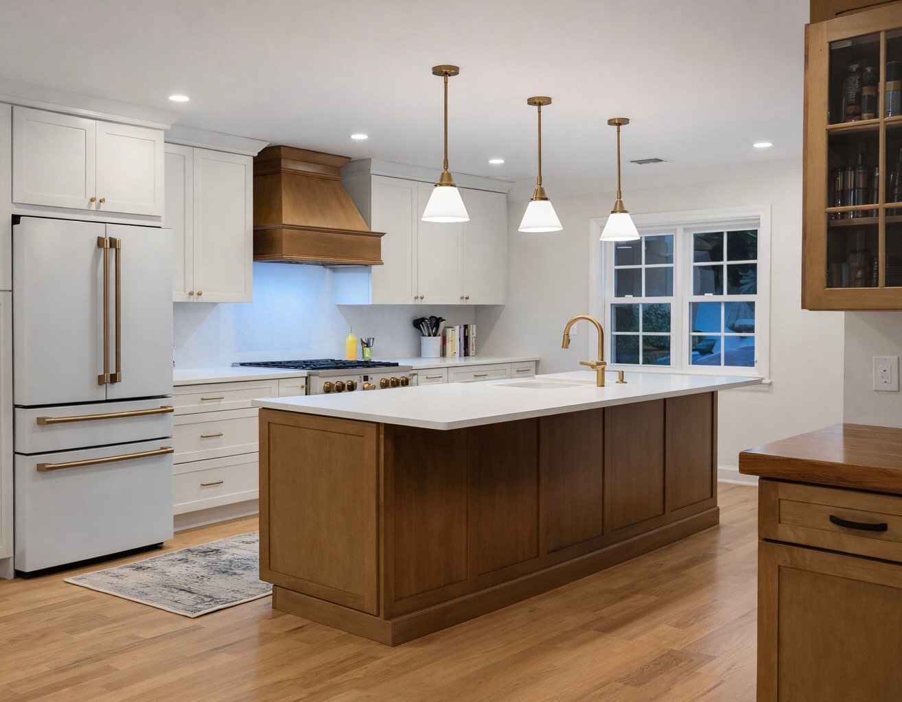 Renovated kitchen with white cabinets, wood island, and brass pendant lighting