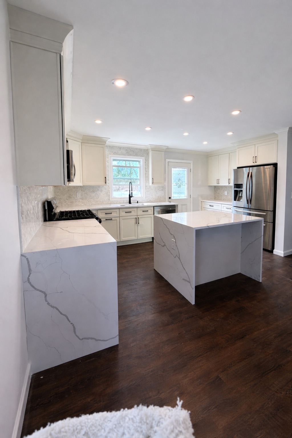 Open kitchen with marble-look waterfall counters and dark wood floors
