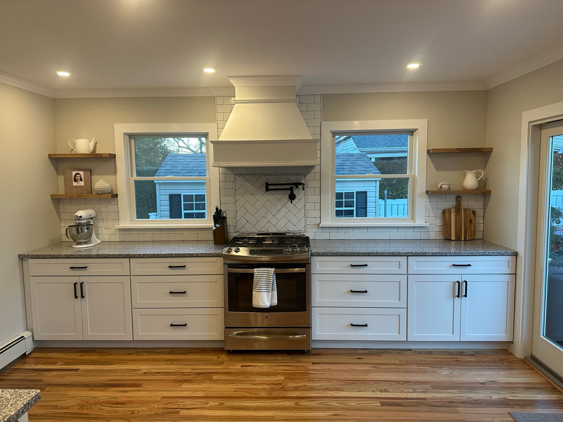 Renovated kitchen with white cabinetry, subway tile, and custom range hood