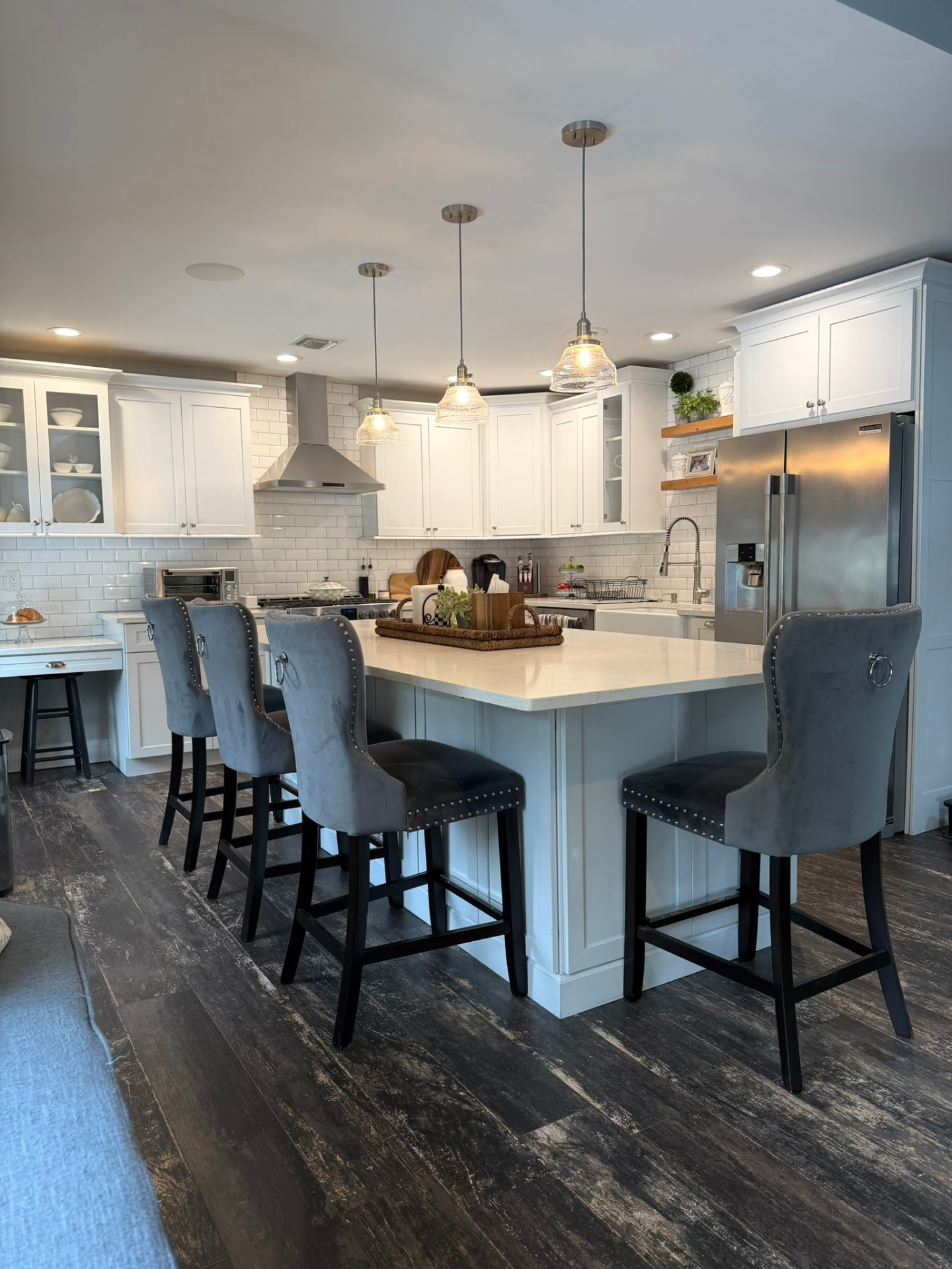 White kitchen with large island, pendant lights, and dark wood floors